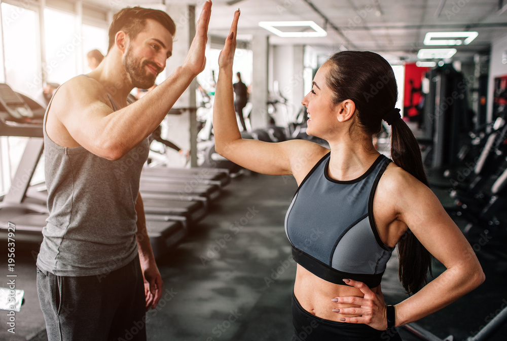 1000_F_195637927_WfYRtfPcO20UoqBpO417b9T0x2IWydEK | Inside Out Fitness Man and woman in a gym high-fiving, smiling, with treadmills and fitness equipment in the background.