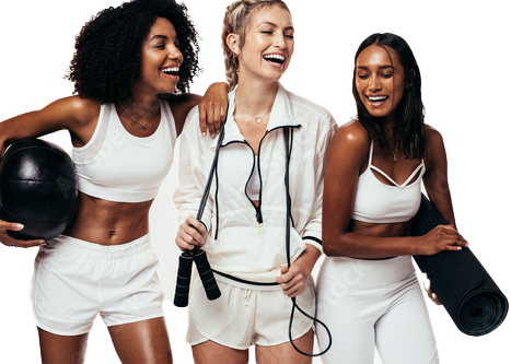 Three women in gym wear laughing together, each holding fitness gear (medicine ball, jump rope, yoga mat).