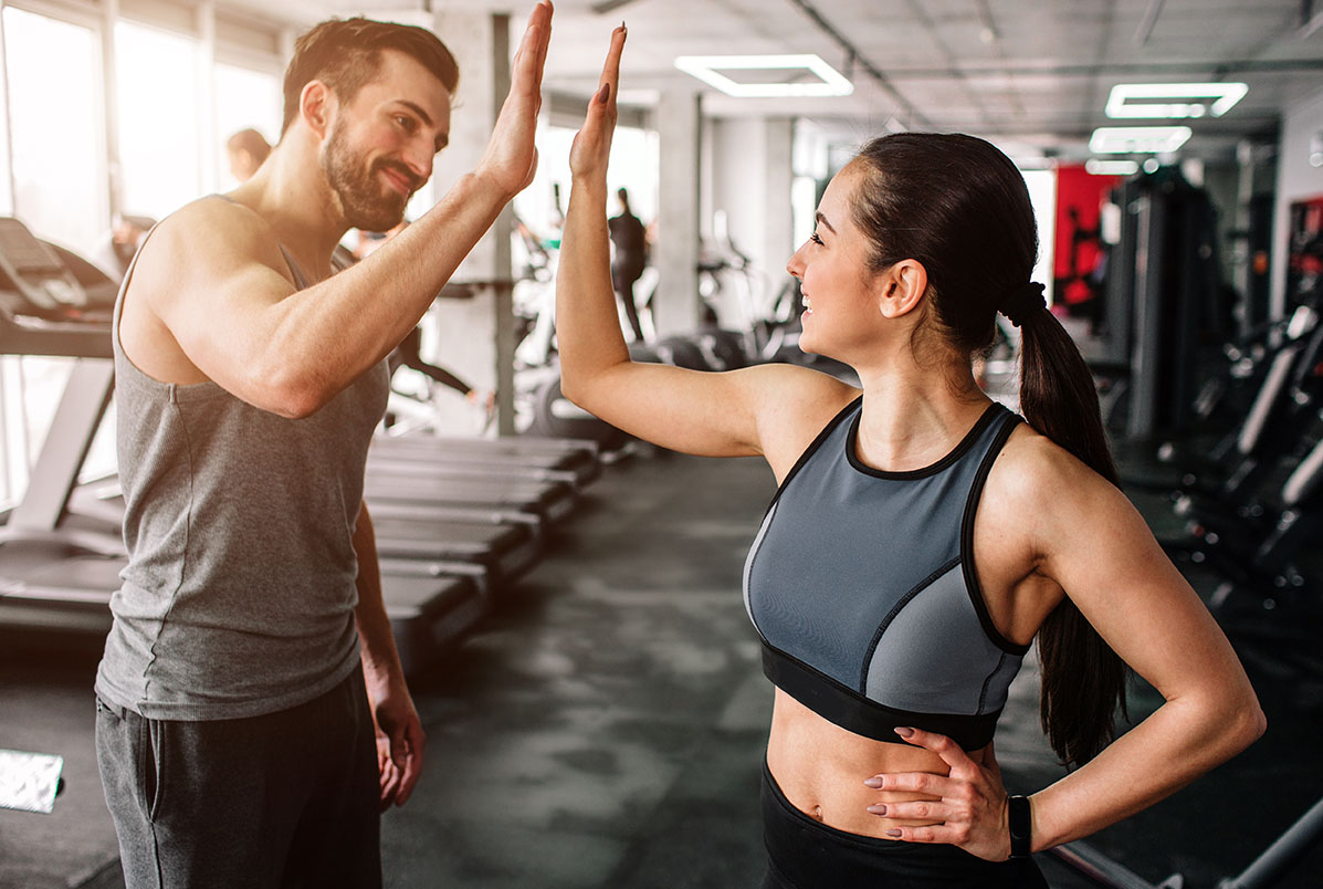 Man and woman in a gym high-fiving, smiling after a workout in athletic wear on a sunny day in the gym.